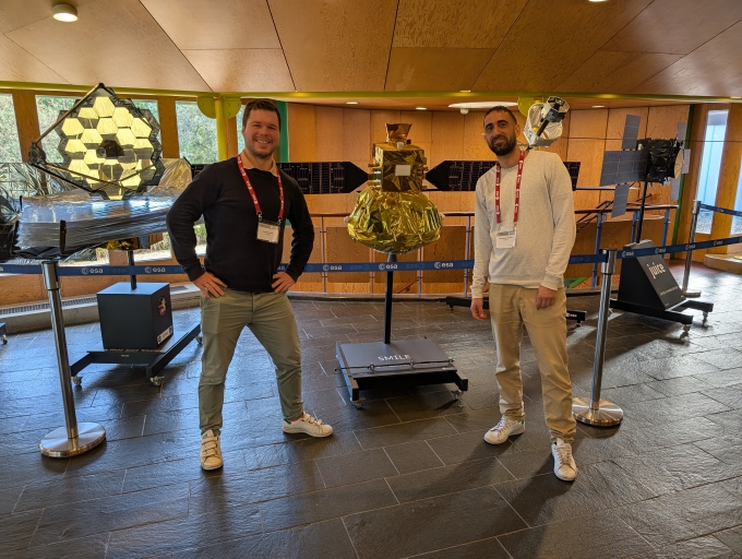 Co-authors of the Ka-Band Choke Ring paper posing in front of some of the satellites models exposed during the ESA Antenna Workshop. From left to right: Quentin Lamotte, Harris Stoumpos.